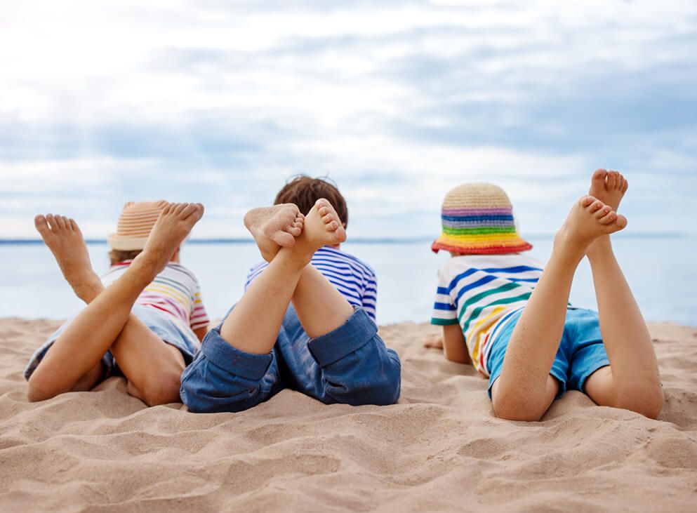 3 kinder liegen am Strand im Sand